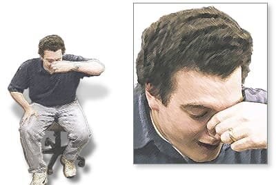 An illustration shows a man seated, pinching the soft part of his nose just above the nostrils, illustrating what to do for a nosebleed.